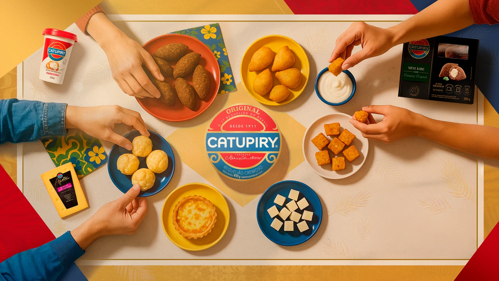 Mesa vista de cima com pratos de kibe, coxinha, pão de queijo, quiche e queijos, mãos pegando os petiscos e o requeijão Catupiry ao centro