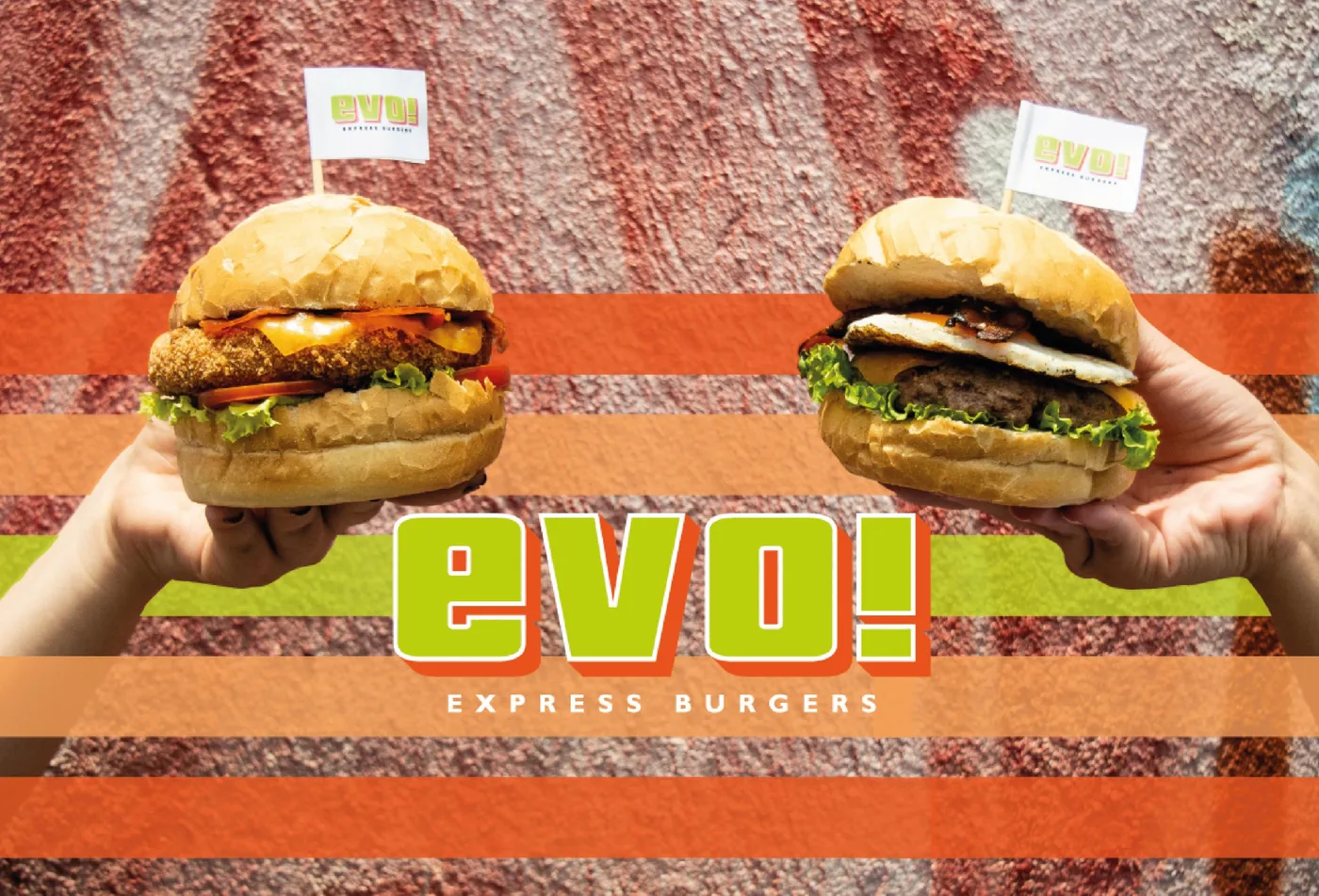 Dois hambúrgueres da EVO Express Burgers segurados no alto, com bandeirinhas da marca, sobre uma parede colorida e faixas laranja e verde