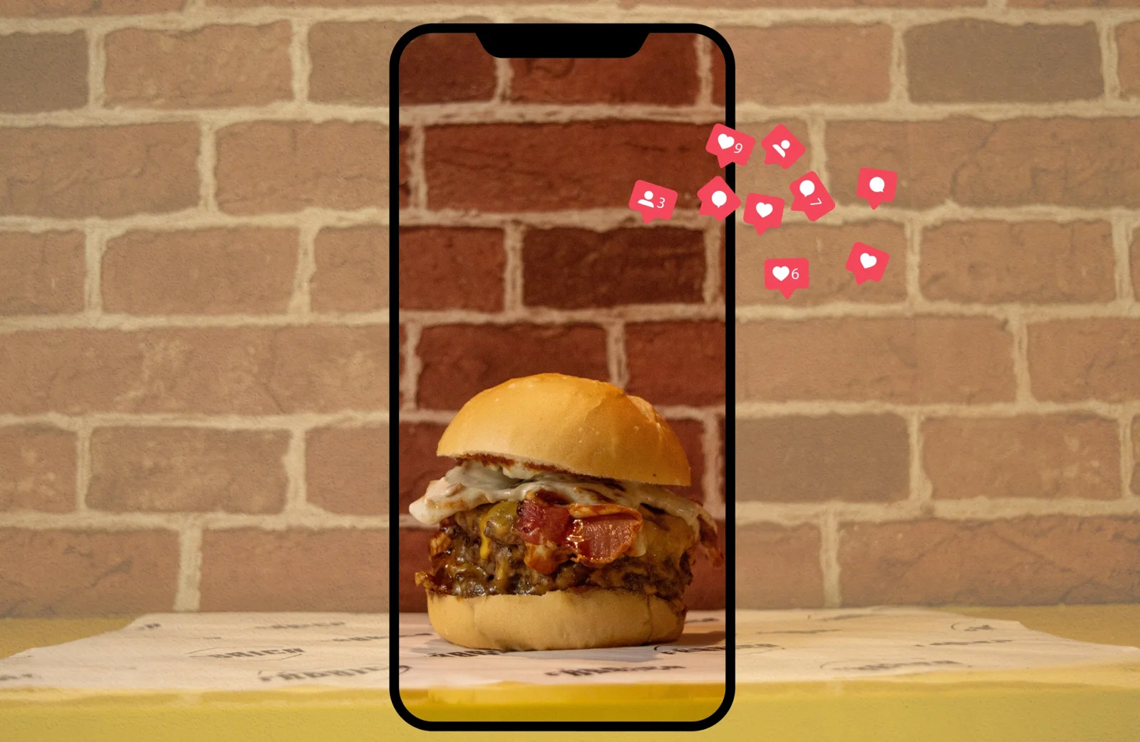 Hambúrguer da Fábrica dentro de uma moldura de celular, com ícones de curtidas, comentários e seguidores do Instagram saindo da tela
