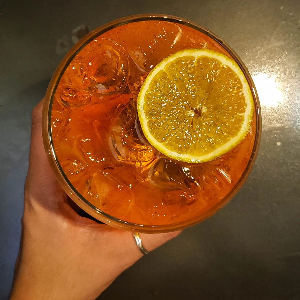Drink laranja com gelo e rodela de limão, visto de cima, segurado por uma mão