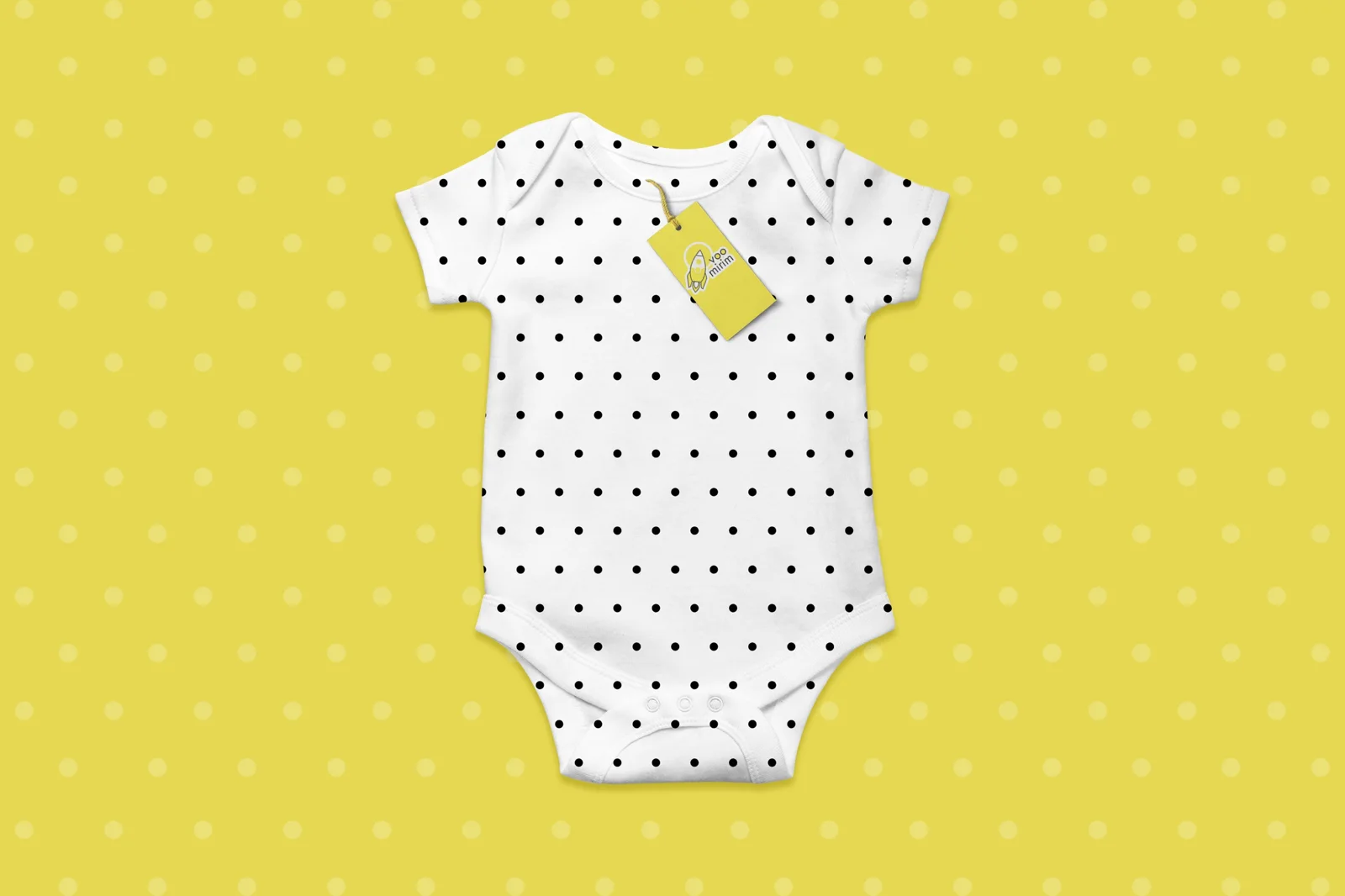 Body de bebê branco com bolinhas pretas e tag amarela Voo Mirim, sobre fundo amarelo