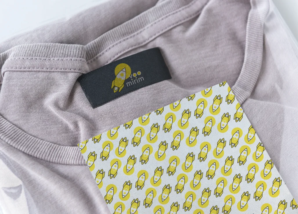 Gola de camiseta com etiqueta preta Voo Mirim e um cartão com o padrão de foguetes